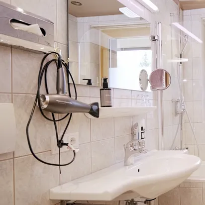 Modern tiled bathroom with bathtub, wall-mounted sink, towel radiator and natural light